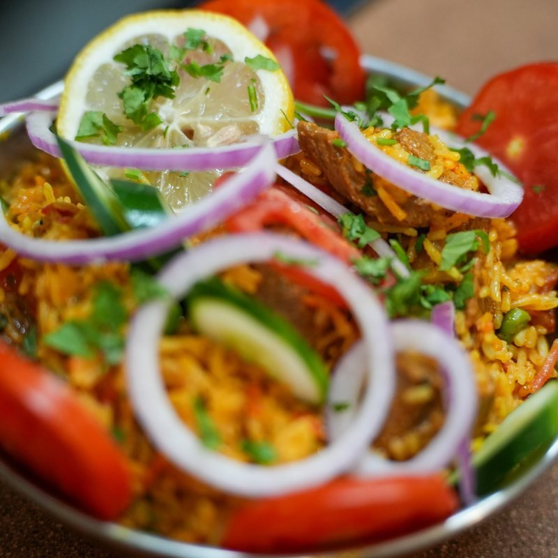 A garnished biriyani with rice, salad and lemon